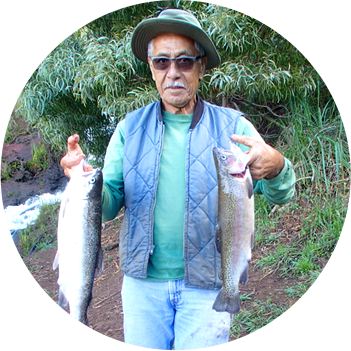 A man wearing blue vest and hat holding a fish in each hand.